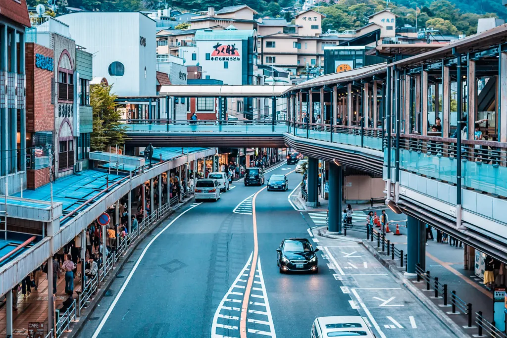 View of the bustling street near Hakone Yumoto station with pedestrians, vehicles, and surrounding buildings under a clear sky.