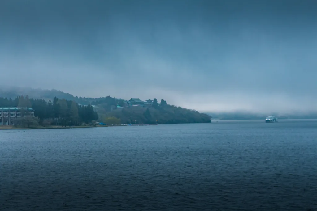 Serene Lake Ashinoko in Hakone with a misty backdrop and a boat sailing across the calm waters.