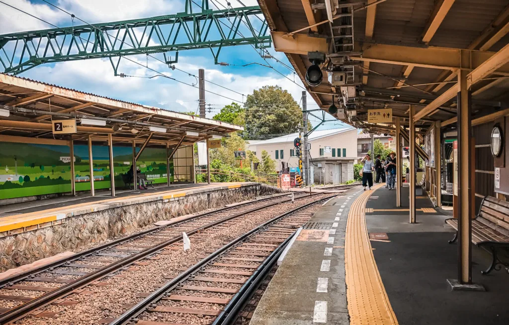 Chokoku-no-Mori station platform in Hakone with empty train tracks, overhead structures, and waiting passengers.