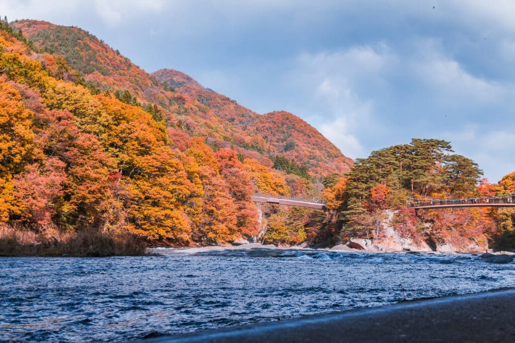Fukiware Falls near Nikko with vibrant autumn leaves in the background and a bridge crossing the nearby area.