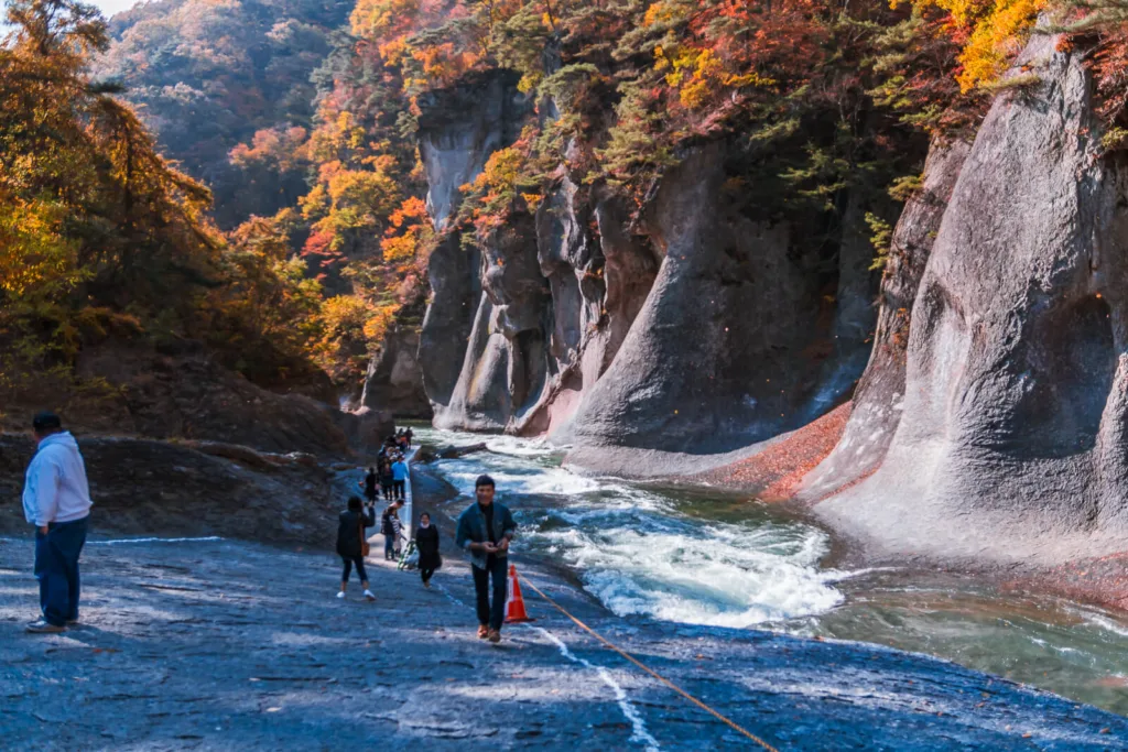 Near Fukiware Falls in Nikko, with autumn leaves in the background and a riverbed showing a large crack eroded by water.