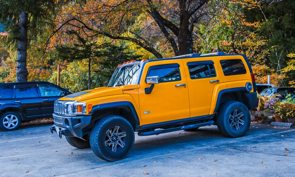 A Hummer parked near the entrance to Fukiware Falls in Nikko, surrounded by vibrant autumn leaves.