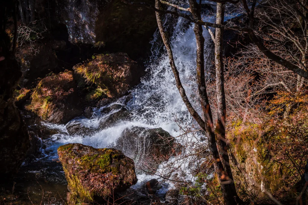 Ryuzu Falls cascading amidst vibrant autumn foliage during daytime, with sunlight highlighting the vivid colors.