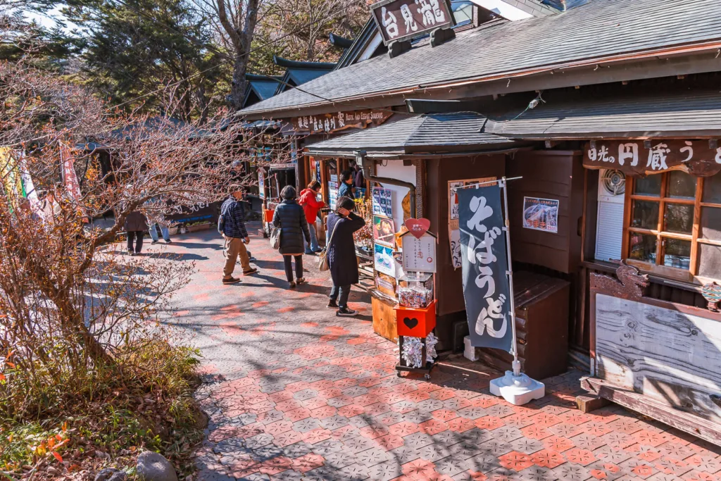 The entrance to the viewing platform of Ryuzu Falls with a souvenir shop and tea house nearby, surrounded by autumn foliage during the daytime.