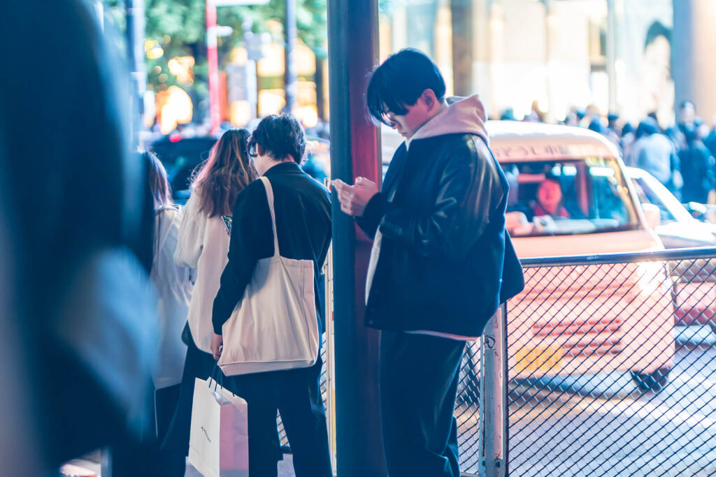 A guy looking at his mobile on the sidewalks of Harajuku.