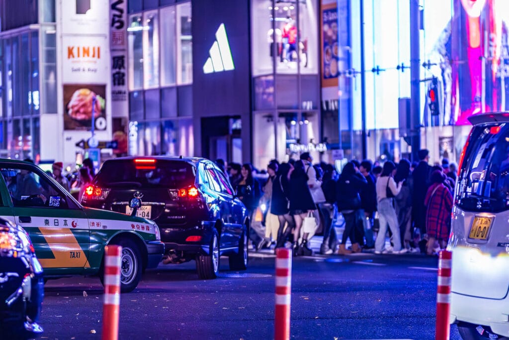 People crossing a street in Harajuku with some cars in the foreground.